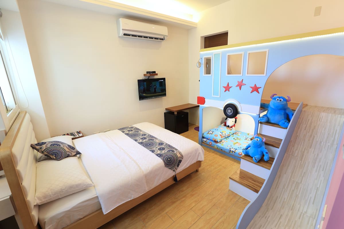 A bedroom with a bed, a TV, a small table, and a playful wall decoration.