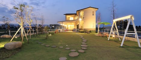 Uma casa moderna com uma entrada bem iluminada, um caminho pavimentado com pedras e um balanço.
