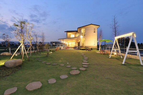 A modern house with a well-lit entrance, a paved pathway with stepping stones, and a swing set.