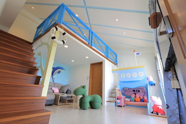 A staircase with wooden steps leading to a blue railing, a green sofa, a pink pig toy, and a children's play area with cartoon characters. - Fun Relax B&B (Wujie)