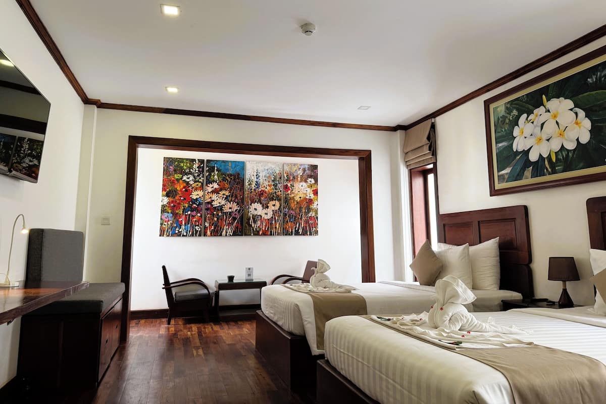 Habitación de hotel con dos camas, un escritorio, una silla, un televisor y un cuadro grande con motivos florales en la pared.