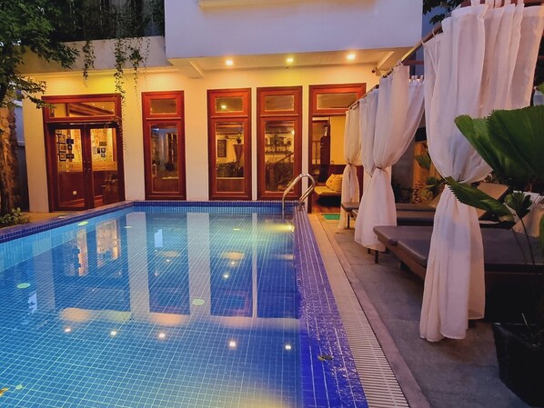 A swimming pool with a tiled edge, adjacent to a building with multiple doors and windows.