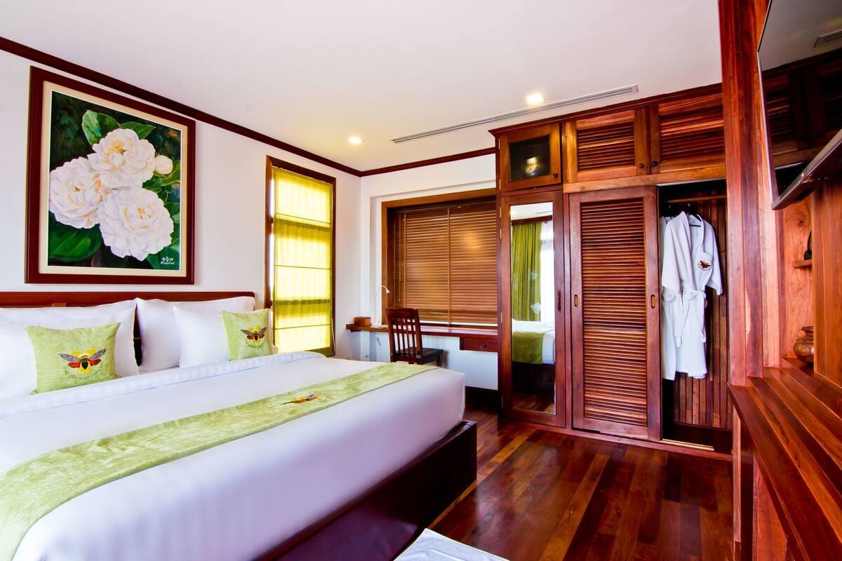 Habitación de hotel con una cama grande, un armario de madera, un escritorio y una ventana con cortinas.