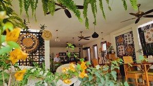 A cozy indoor space with ceiling fans, hanging plants, and a dining area with wicker furniture. - Maison Saiko Angkor Boutique (Siem Reap)