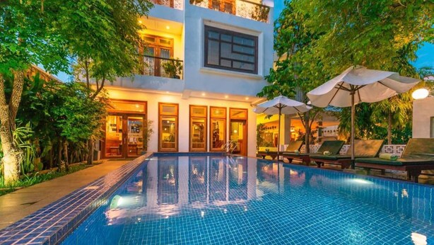 A swimming pool with a tiled edge, surrounded by lounge chairs and umbrellas, and a building with multiple windows and balconies. - Maison Saiko Angkor Boutique (Siem Reap)