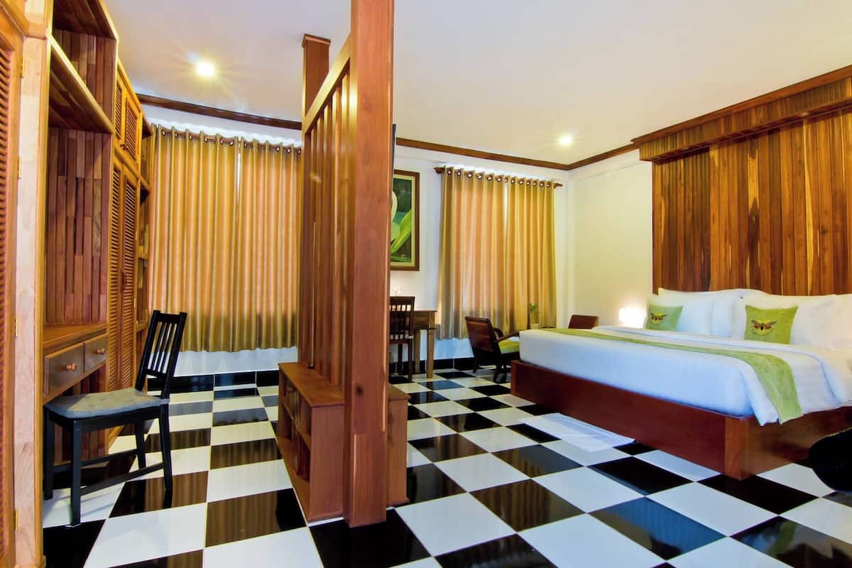 Una habitación de hotel con piso a cuadros, muebles de madera, una cama con almohadas verdes y cortinas.