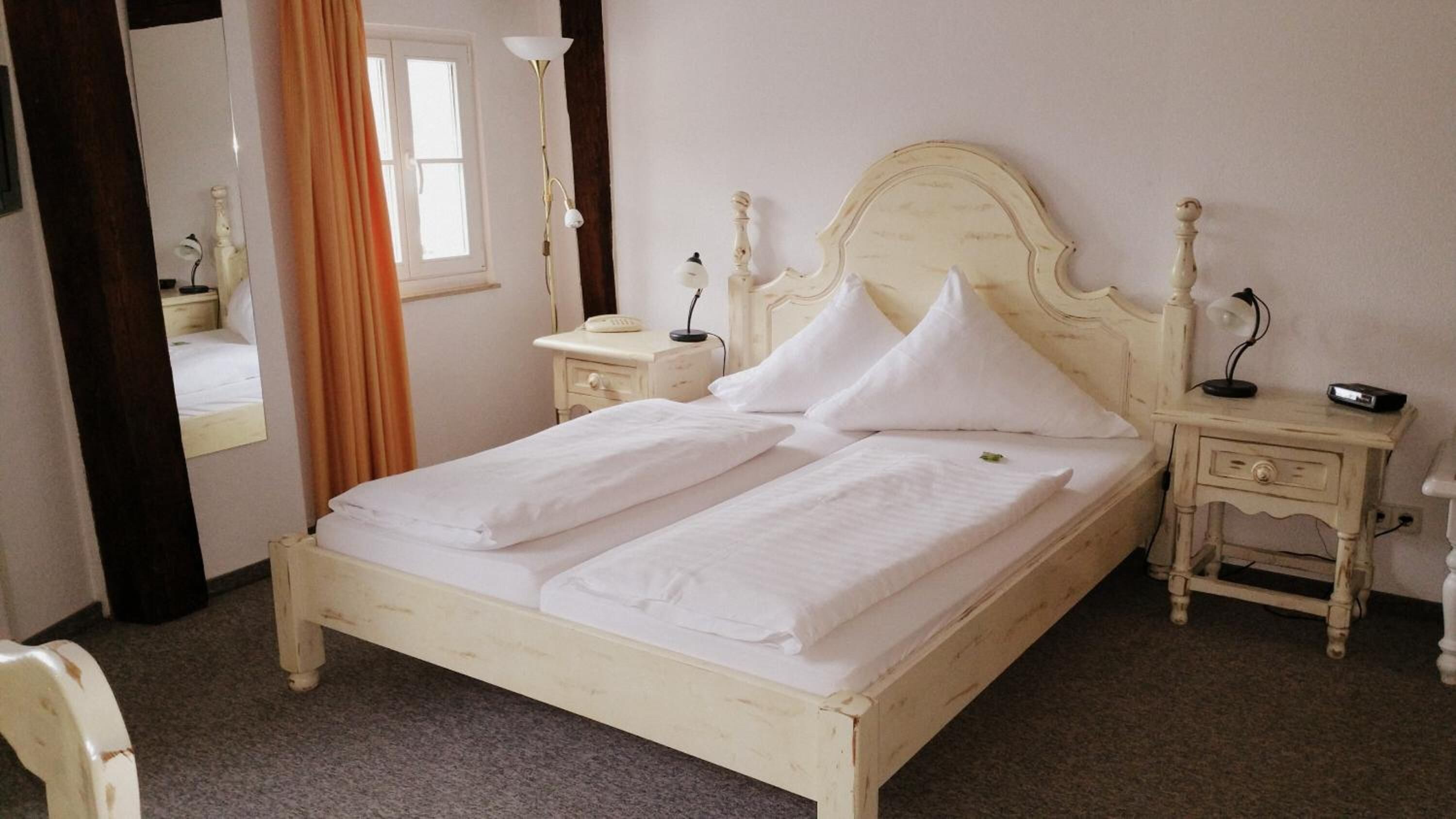 A double bed with white linens, a wooden headboard, bedside tables with lamps, and a mirror on the wall.