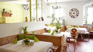 Een restaurant met houten meubels, witte tafellinnen en groene kussens.