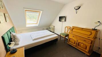 Ein Zimmer mit einem Bett, einem Sessel, einem Schrank, einem Fernseher und einem Fenster.