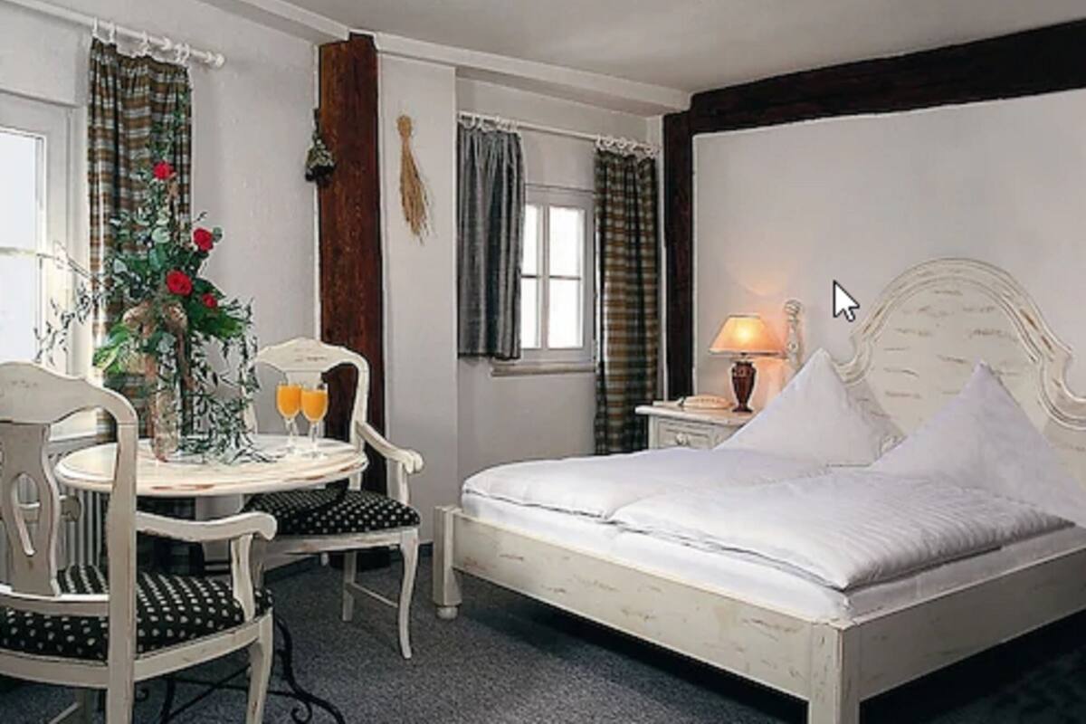 Un dormitorio con una cama, un escritorio con dos sillas, una mesa con un jarrón de flores y una lámpara.