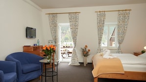 Een slaapkamer met een bed, een blauwe fauteuil, een tafeltje met een bloevas en een televisie aan de muur.