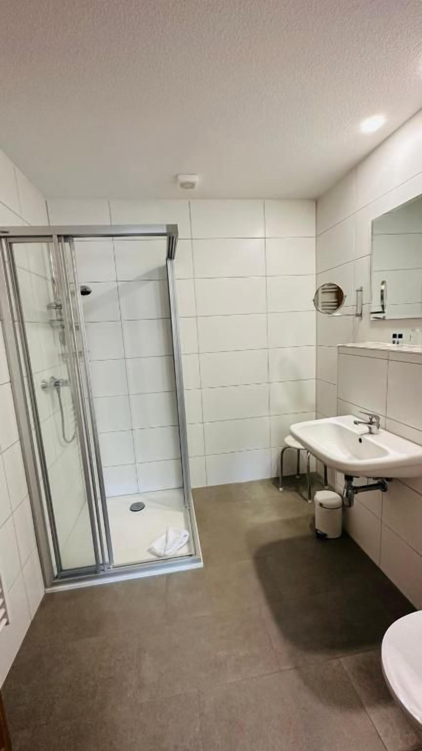 A bathroom with a glass shower enclosure, a sink, and a mirror.
