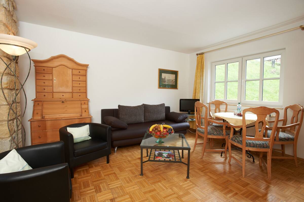 Una sala de estar con un aparador de madera, un sofá, una mesa de centro con un frutero, y un comedor con sillas y una mesa.