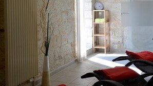 Een kamer met een stenen muur, een radiator, een klok en twee zwarte stoelen met rode kussens.