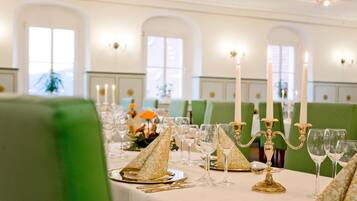 A formal dining setting with tables set for multiple guests, featuring gold-patterned napkins, clear glassware, and white candles.