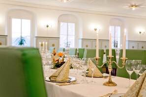 Une salle à manger élégante, avec des tables dressées pour accueillir plusieurs convives, agrémentée de serviettes à motifs dorés, de verres transparents et de bougies blanches.