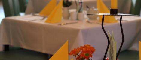 A dining table set with yellow napkins, candles, and a vase with flowers.