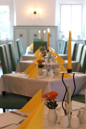 Una mesa de comedor dispuesta con servilletas amarillas, velas y un florero con flores.