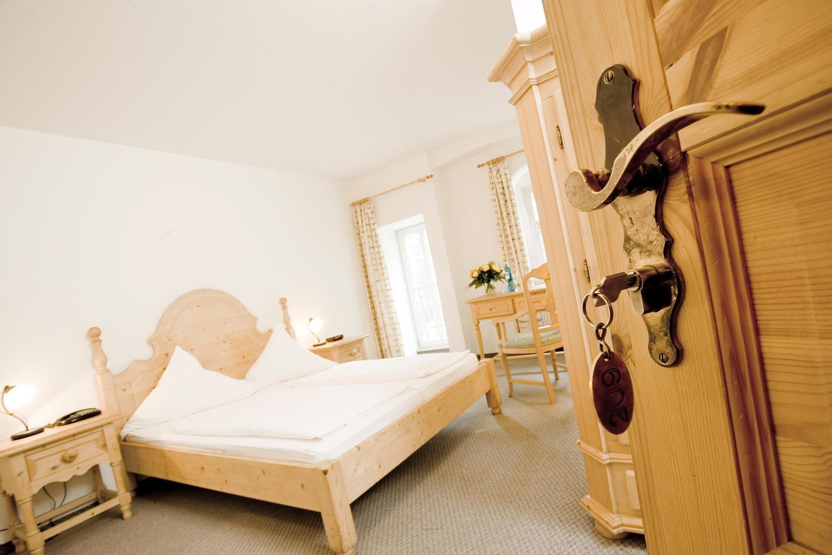 Una cama de madera en una habitación con una mesita de noche, un aparador y un escritorio con una silla.