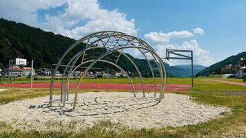 A metal structure resembling a tunnel or arch in a park setting with a red track and houses in the background.