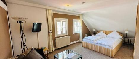 A hotel room with a bed, a small table, a TV, and a radiator.