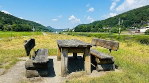 Une table de pique-nique rustique, avec des bancs, installée dans un champ verdoyant, offrant une vue sur une rivière et des collines en arrière-plan.