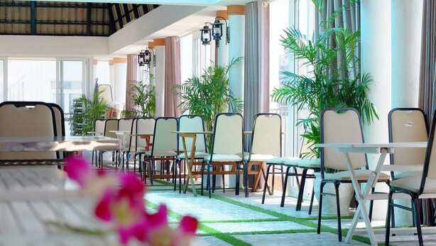 A modern indoor dining area with multiple tables and chairs, large windows, and potted plants.