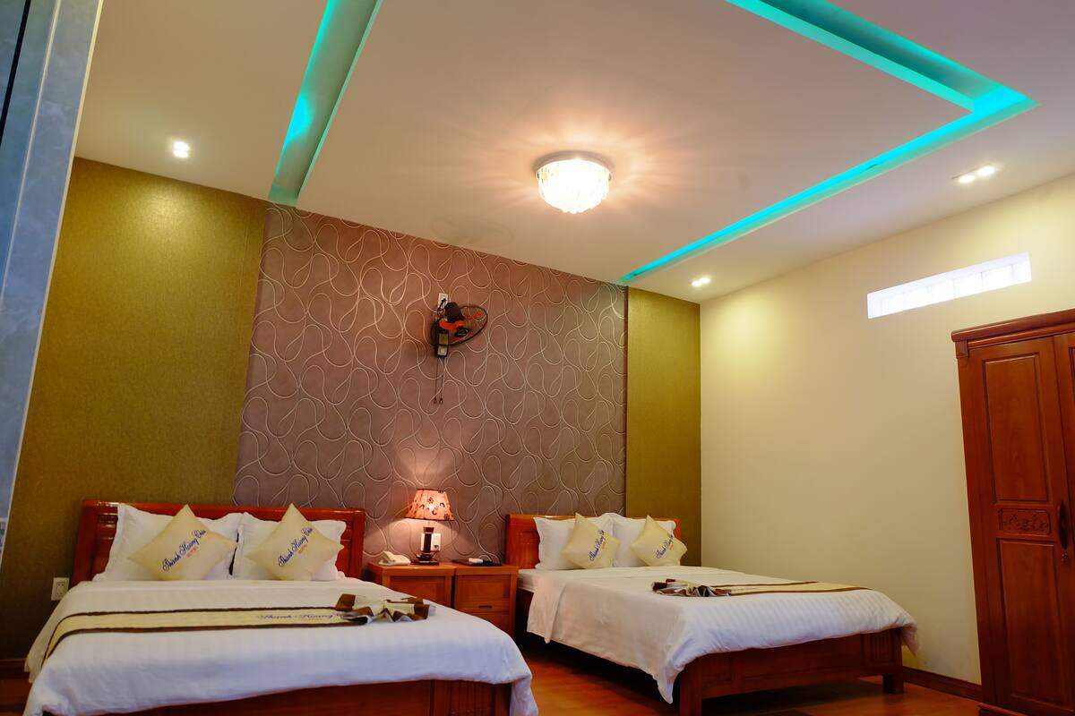 A hotel room with two beds, a nightstand with a lamp, a wall clock, and a wardrobe.