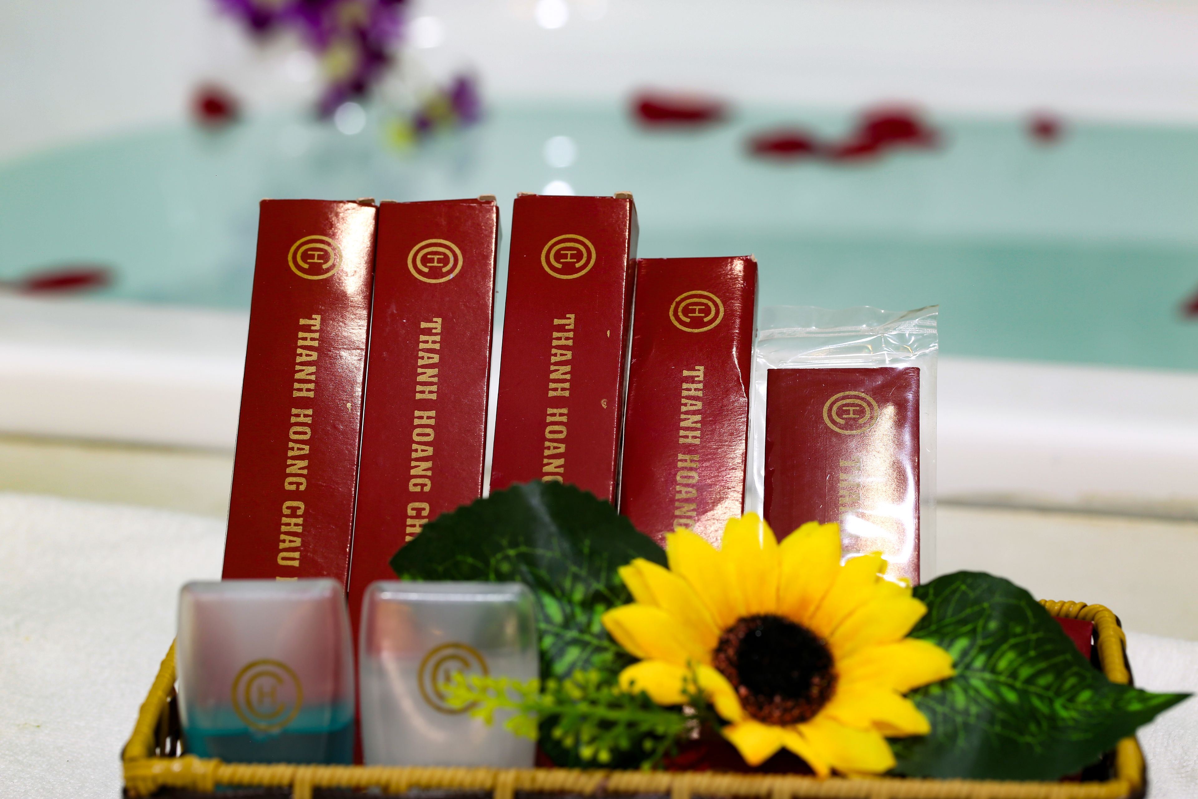 A set of red books titled "THANH HOANG CHAU" and a basket containing a candle, a sunflower, and a small plant.