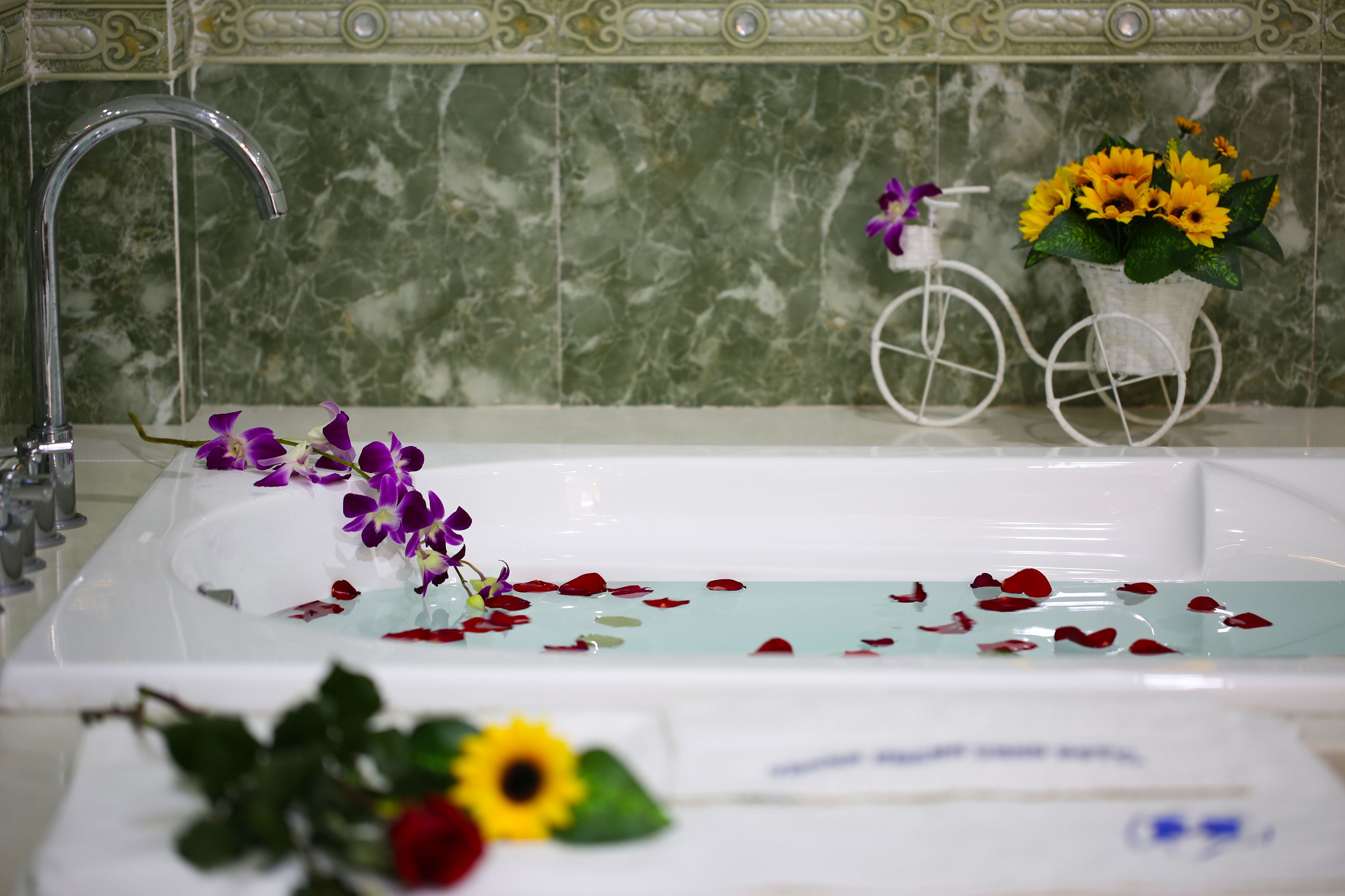 A bathtub with water, flowers, and rose petals.