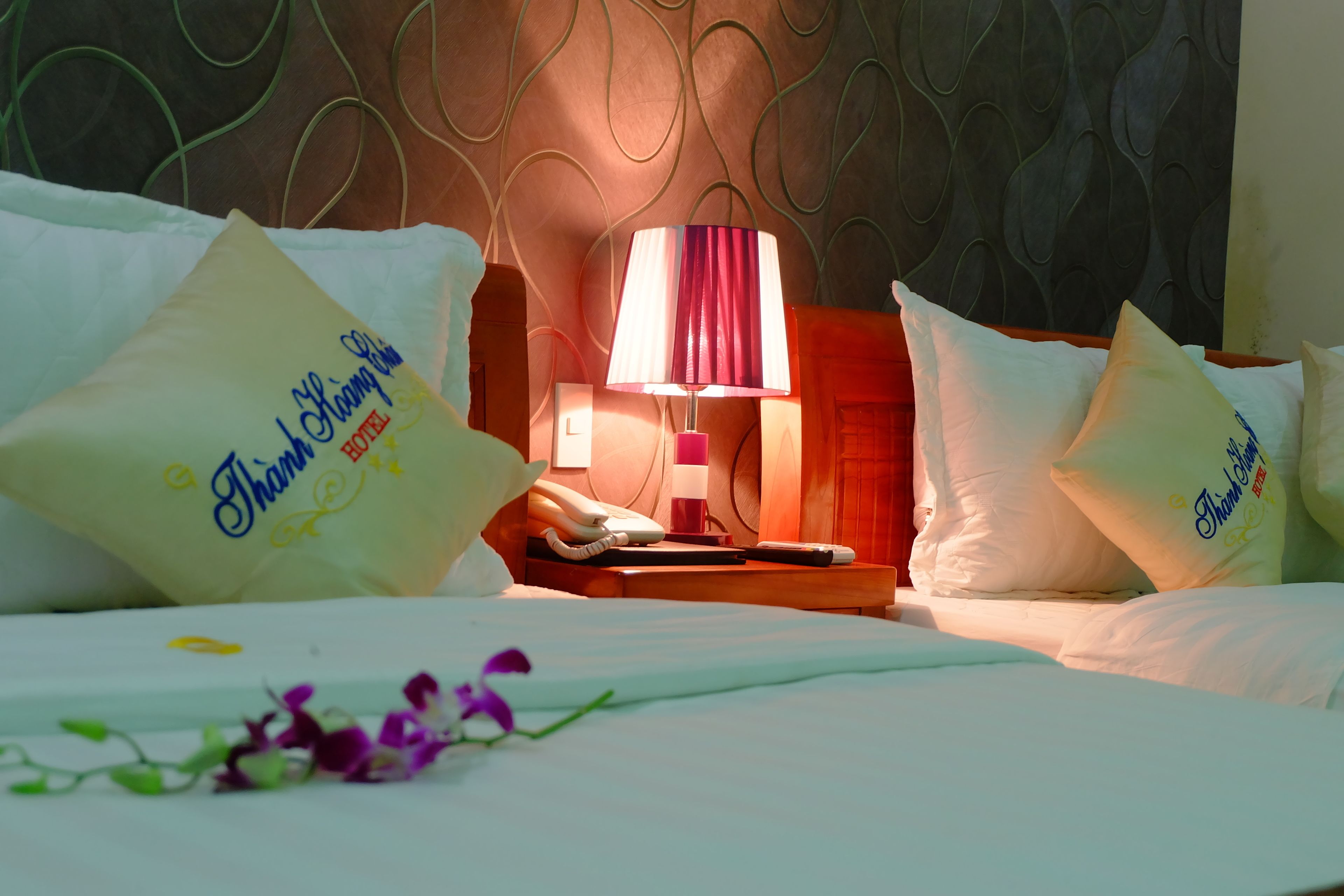Een hotelkamer met een bed, kussens, een nachtkastje, een lamp en een telefoon.