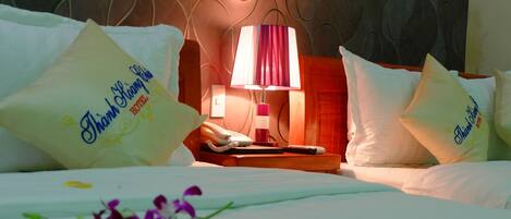 Een hotelkamer met een bed, kussens, een nachtkastje, een lamp en een telefoon.