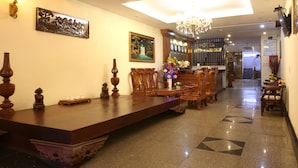 A hotel lobby with a long reception desk, wooden chairs, a chandelier, and artwork on the walls.