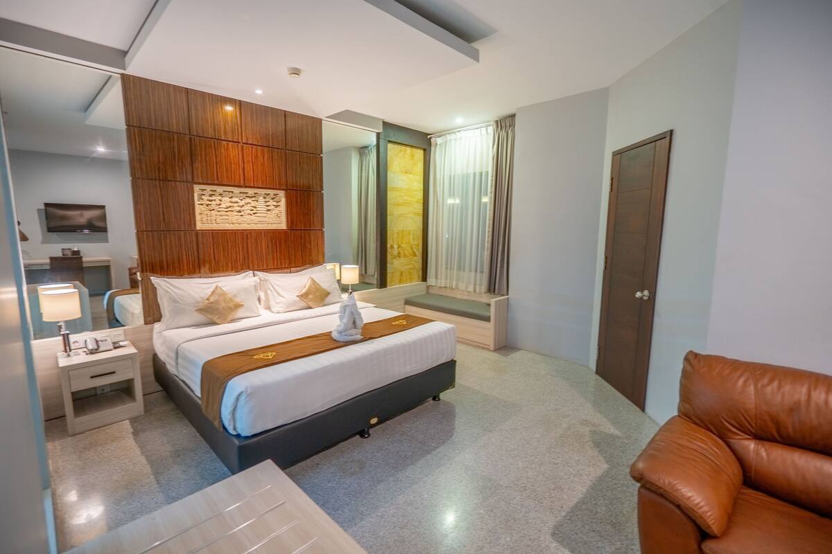 Una habitación de hotel moderna con una cama grande, mesitas de noche, un espejo y un sillón de cuero marrón.