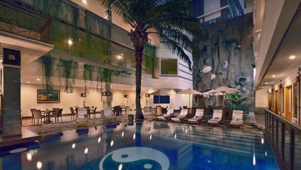 An indoor swimming pool with a yin-yang symbol, lounge chairs, and a palm tree. - Famous Hotel Kuta (Tuban)
