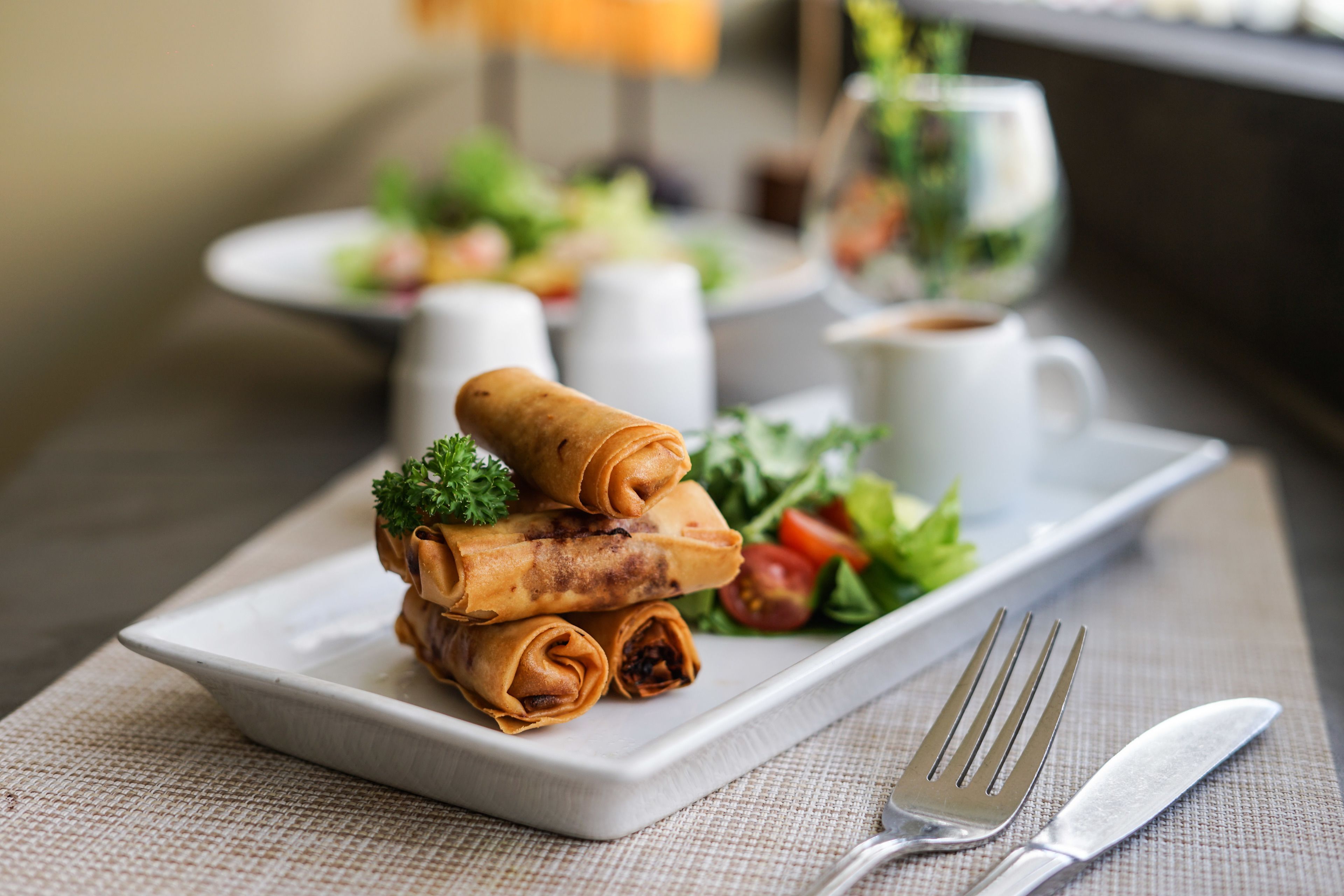 A plate of rolled spring rolls with a side salad and a cup of coffee on a table.
