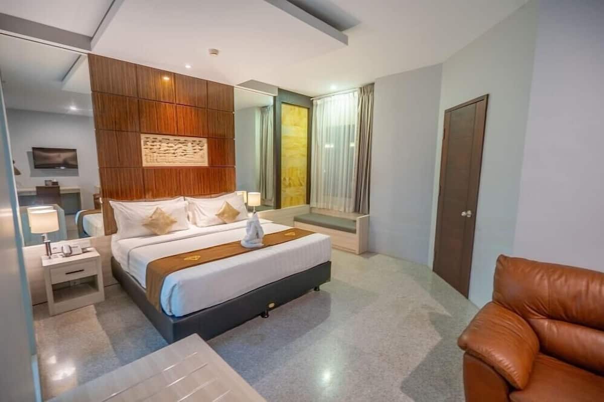 Una habitación de hotel moderna con una cama, mesitas de noche, un espejo, un televisor y un sillón de cuero.