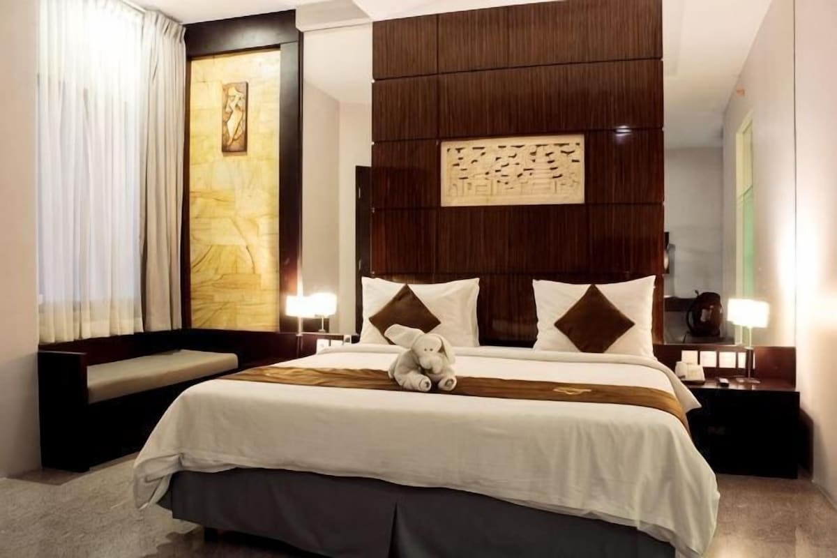 A hotel room with a large bed, a bench, a nightstand, and a wall-mounted artwork.