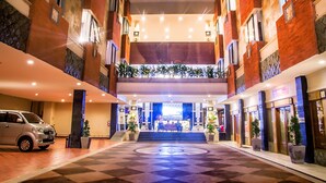A hotel lobby with a checkered floor, a reception desk, and a staircase leading to upper floors. - Famous Hotel Kuta (Tuban)