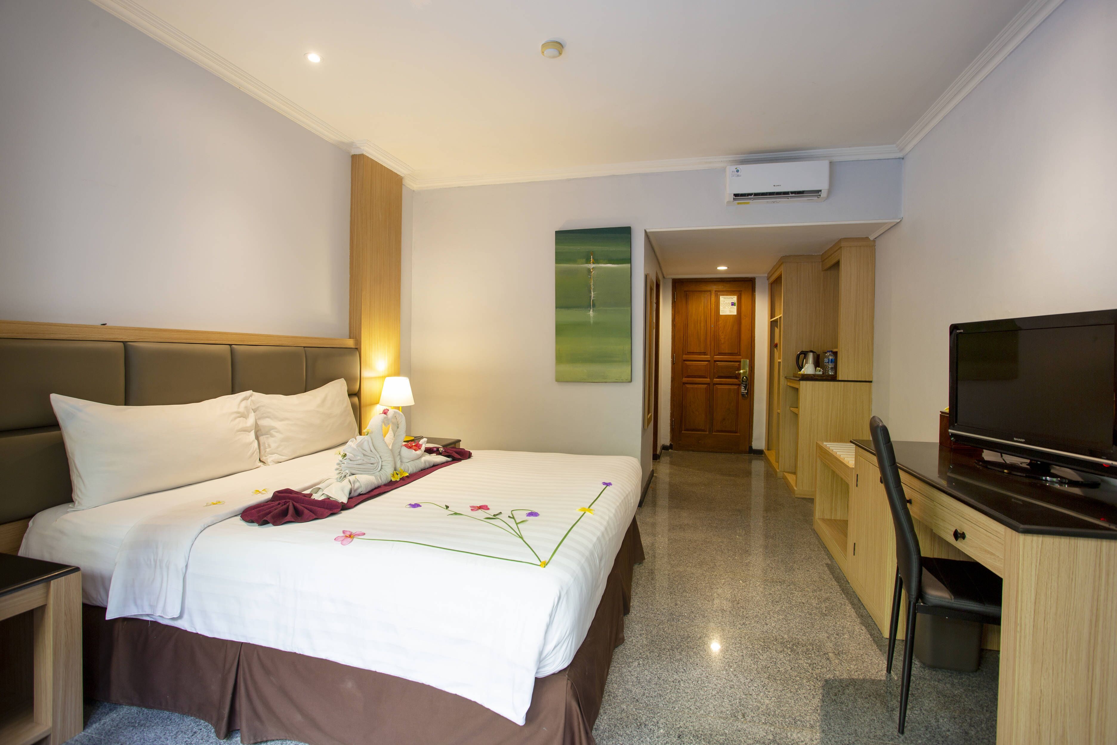 A hotel room with a bed, bedside table, lamp, and a television.