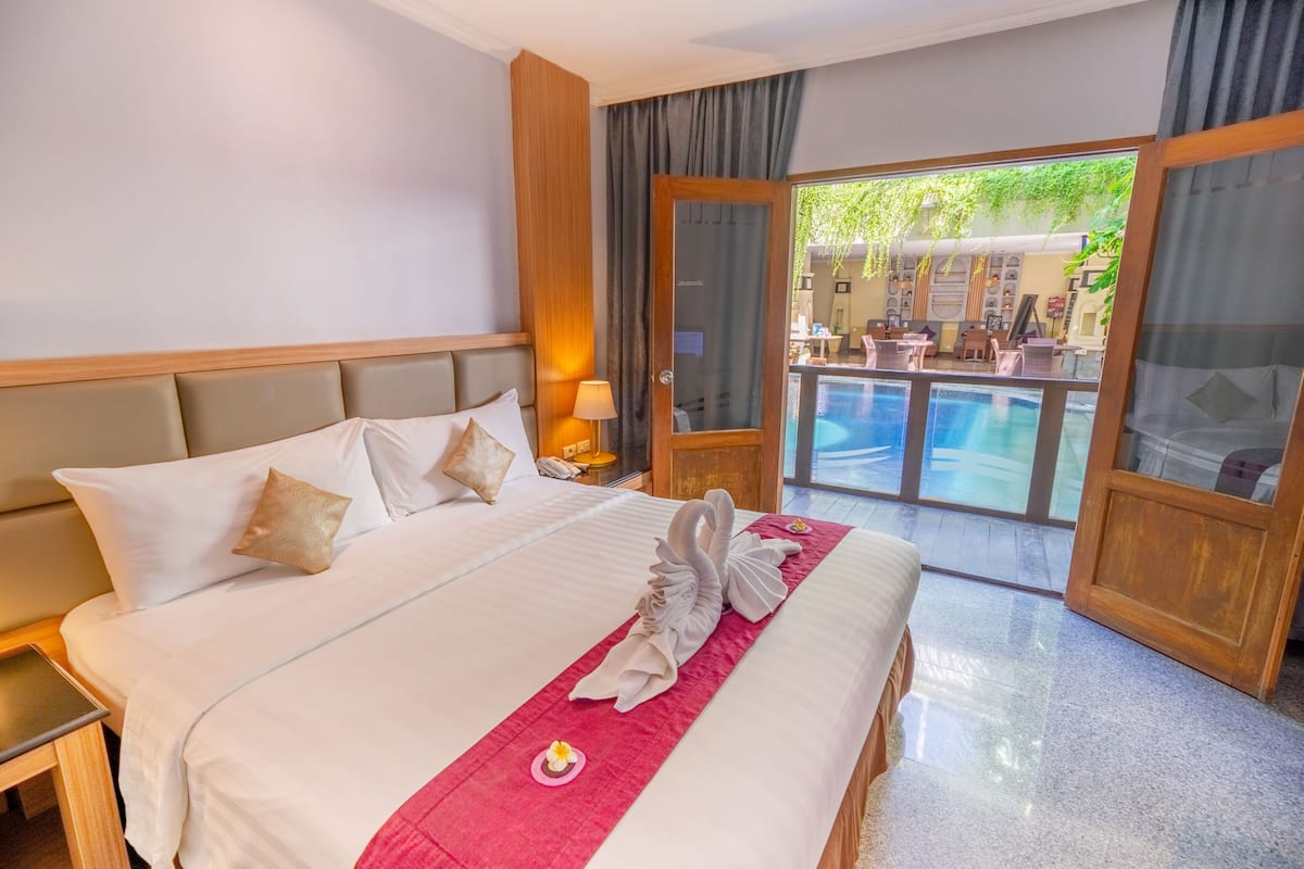 Habitación de hotel con una cama grande, una mesita de noche, una lámpara y vistas a una piscina al aire libre.