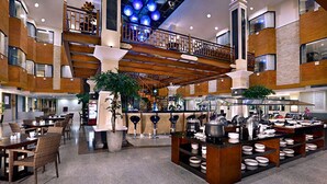 A spacious hotel lobby with multiple dining areas, a central buffet, and a staircase leading to an upper level. - Famous Hotel Kuta (Tuban)