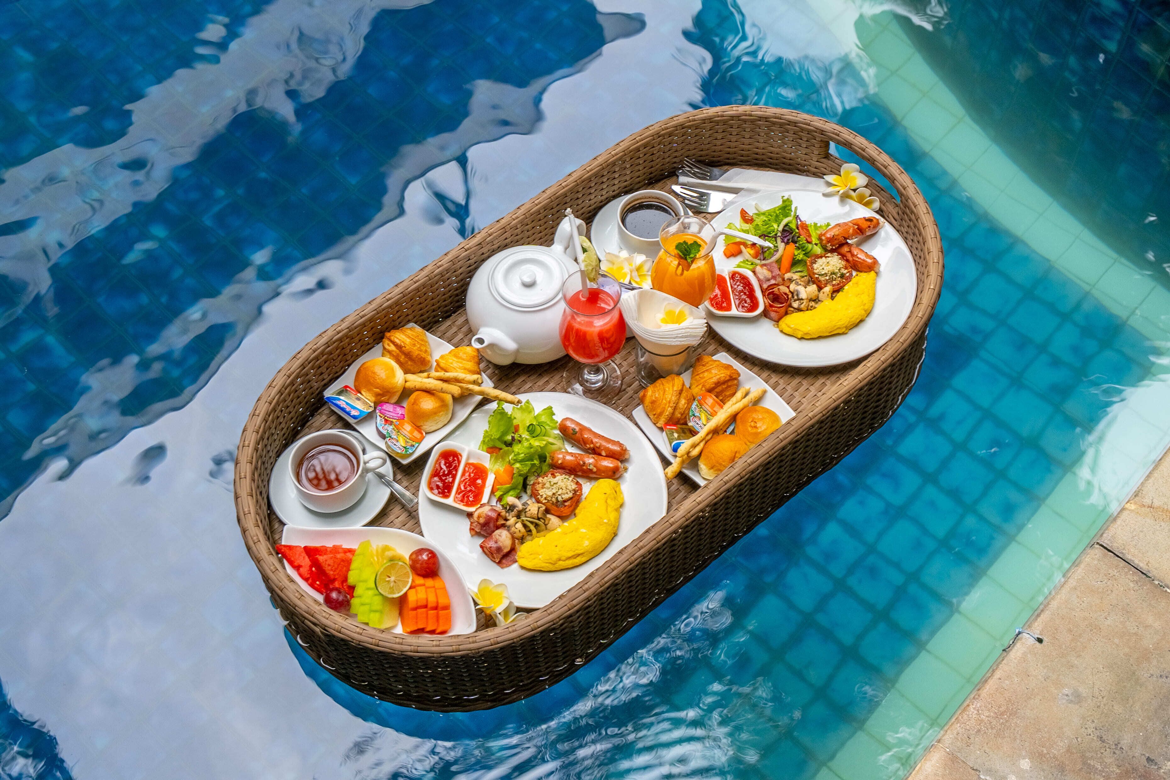 A floating dining setup with a variety of food items and drinks, including a teapot, plates of food, and a basket.