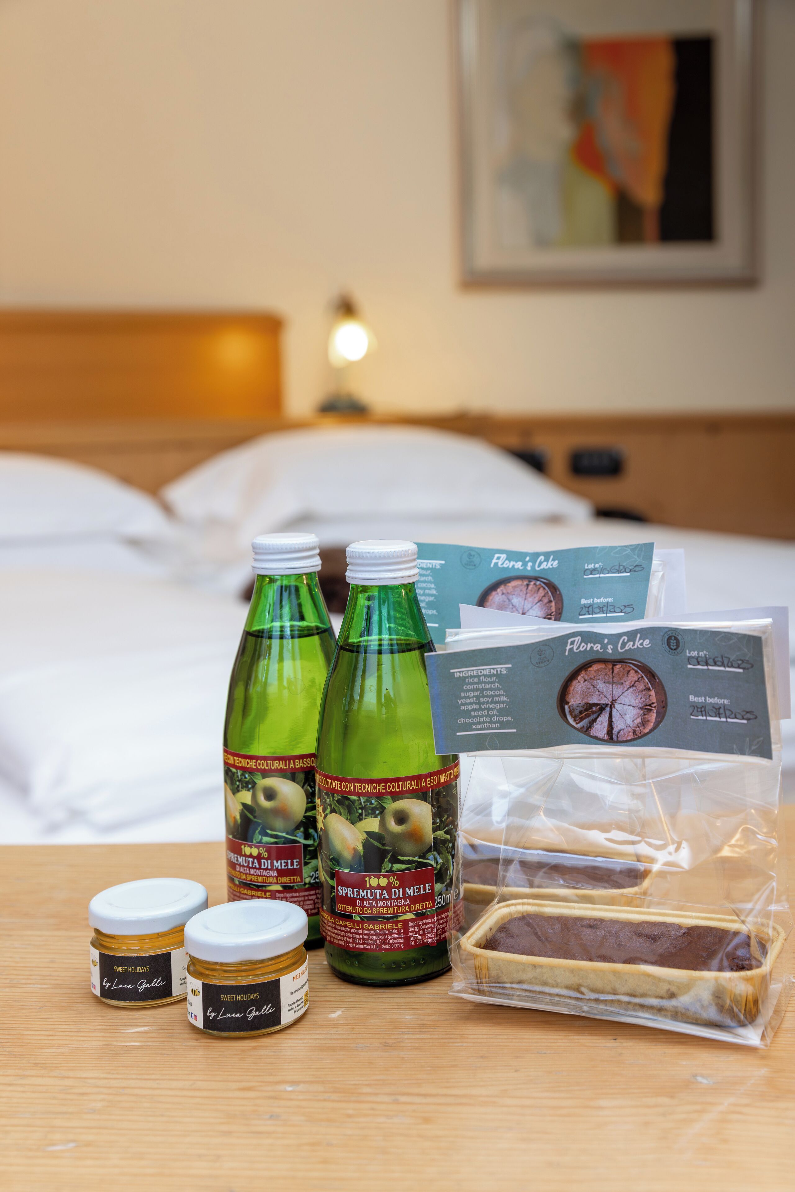 A hotel room with a bed, a table with food items, and a painting on the wall.