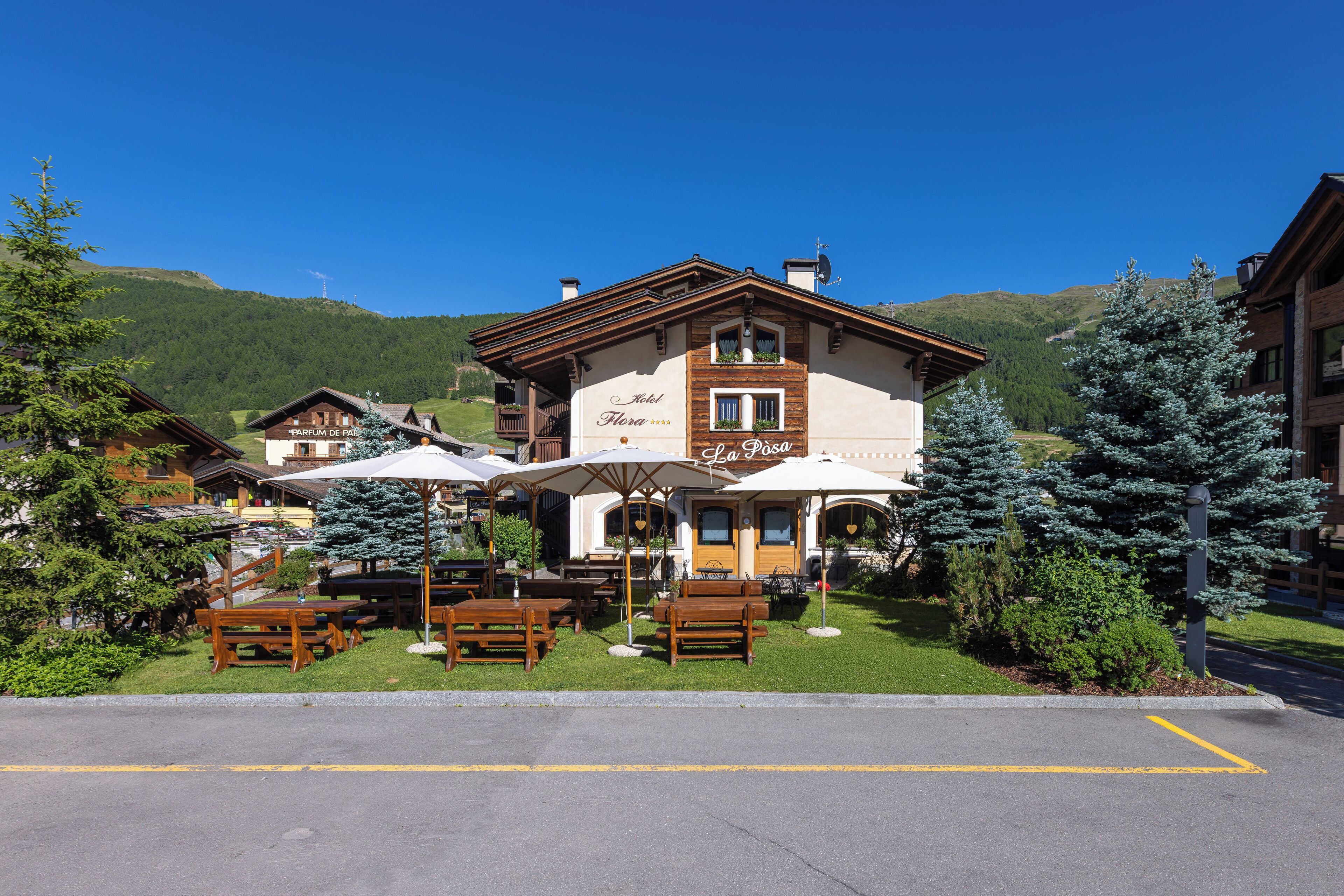 A hotel with outdoor seating, a sign reading "Hotel La Fossa," and a mountainous backdrop.