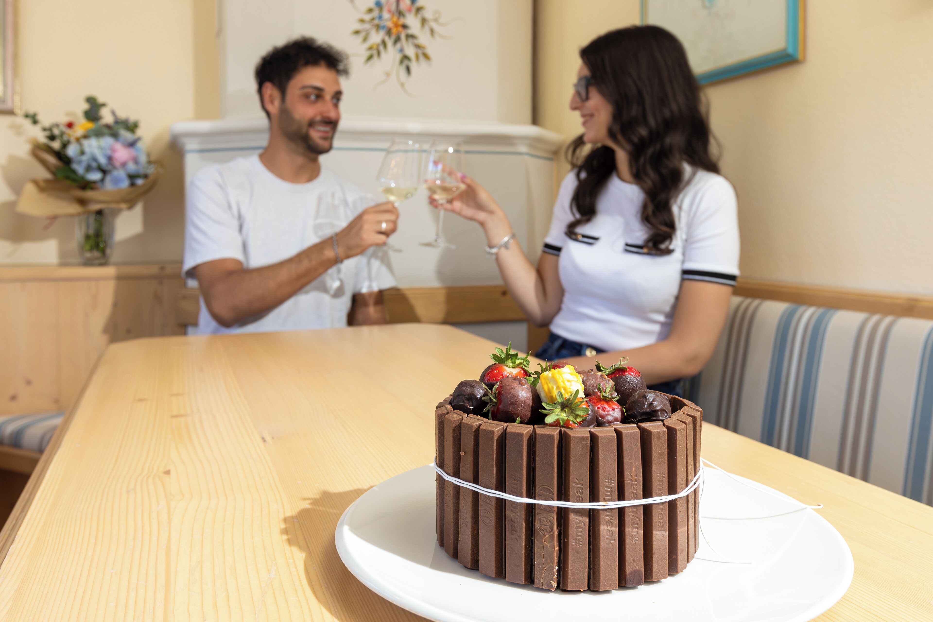Un gâteau au chocolat rond, garni de fraises et accompagné d’une tablette de chocolat, le tout présenté sur une assiette blanche posée sur une table en bois.