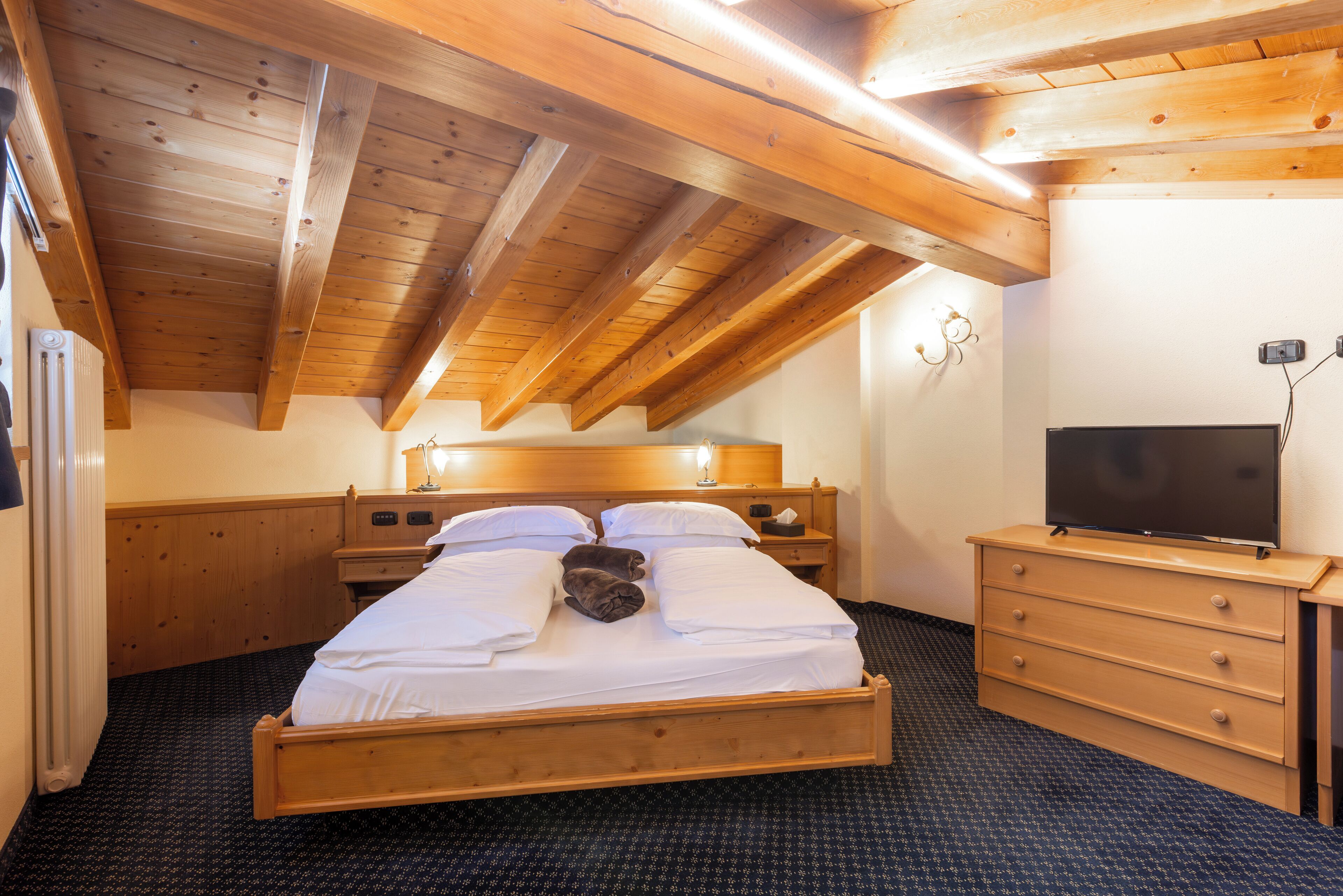 A wooden-framed bedroom with a bed, bedside tables, a dresser, and a television.