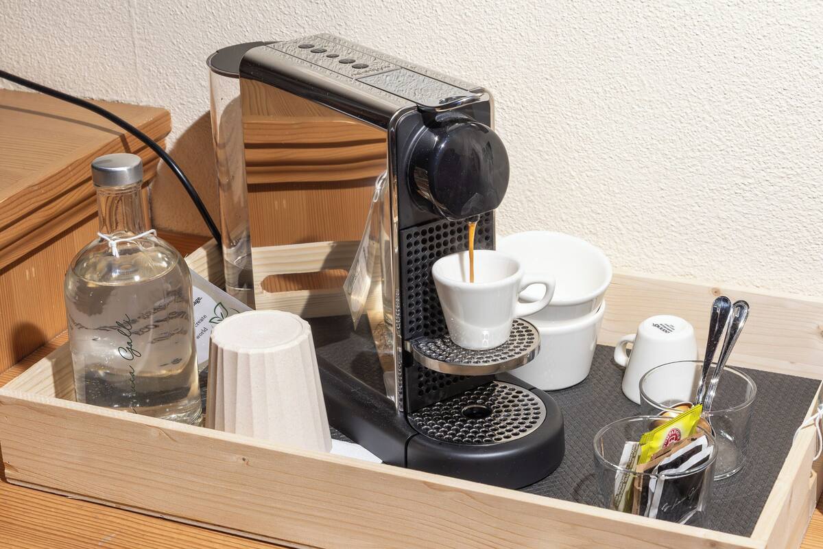 A wooden tray with a coffee machine, cups, a bottle, and a spoon.