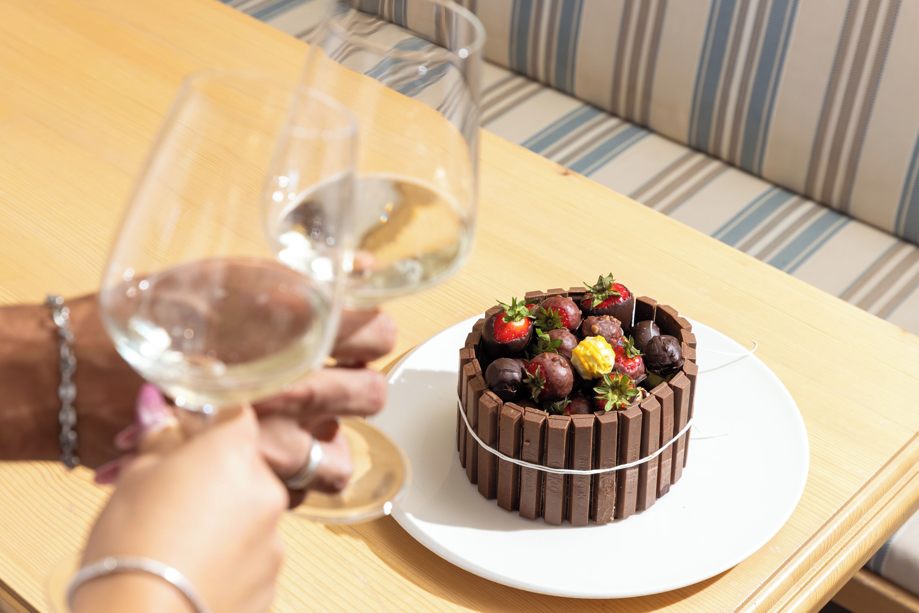 Un pastel de chocolate redondo con fresas y otras frutas sobre un plato blanco en una mesa de madera.