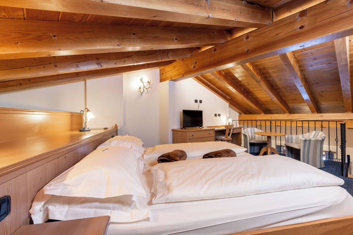 A wooden ceiling with exposed beams, a bed with white linens, a desk with a computer, and a chair.
